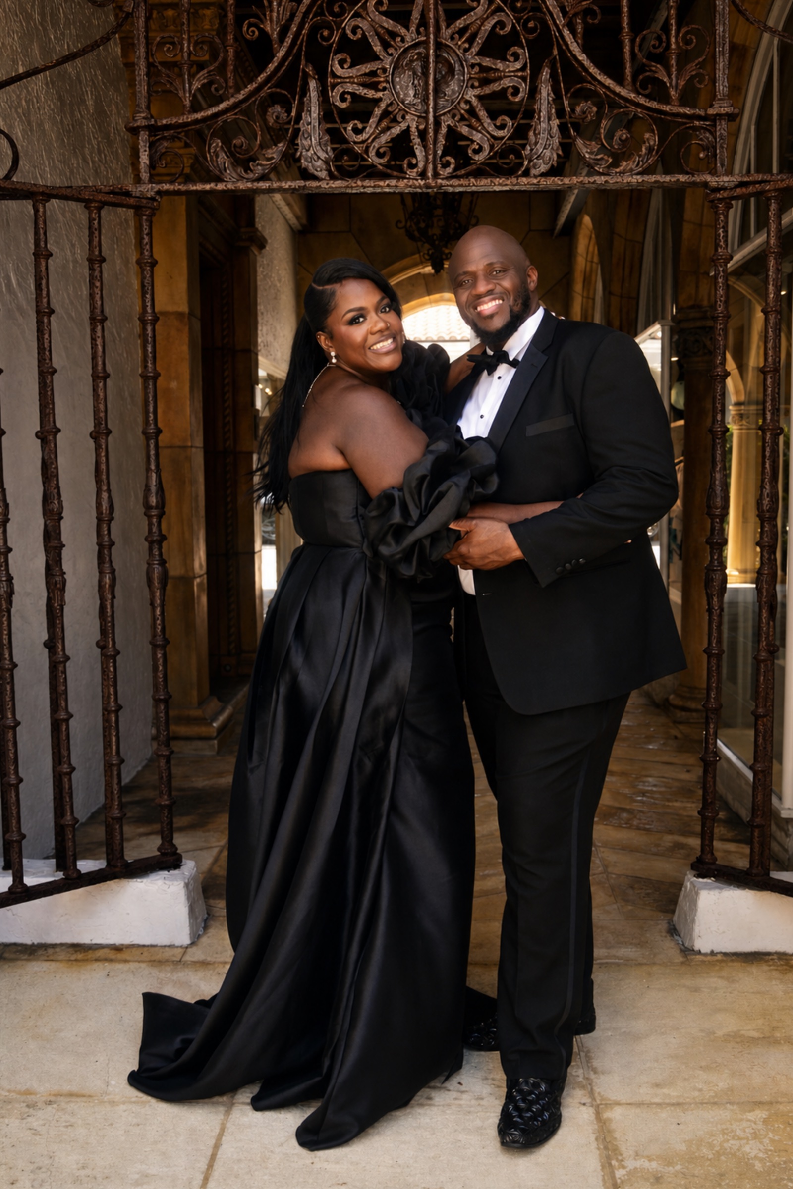 Wilda and Sean smiling together beneath ornate gates